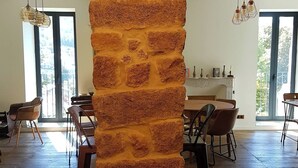 A spacious room with a large brick column, wooden flooring, and a dining area with chairs and a table. - A Bella Scusa (Bastelica)