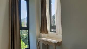 A room with two windows, one with brown curtains and another with white curtains. There is a small white table with a curved design next to the windows.