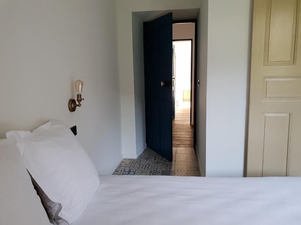 A hotel room with a bed, a wall-mounted light fixture, and a door leading to a hallway.