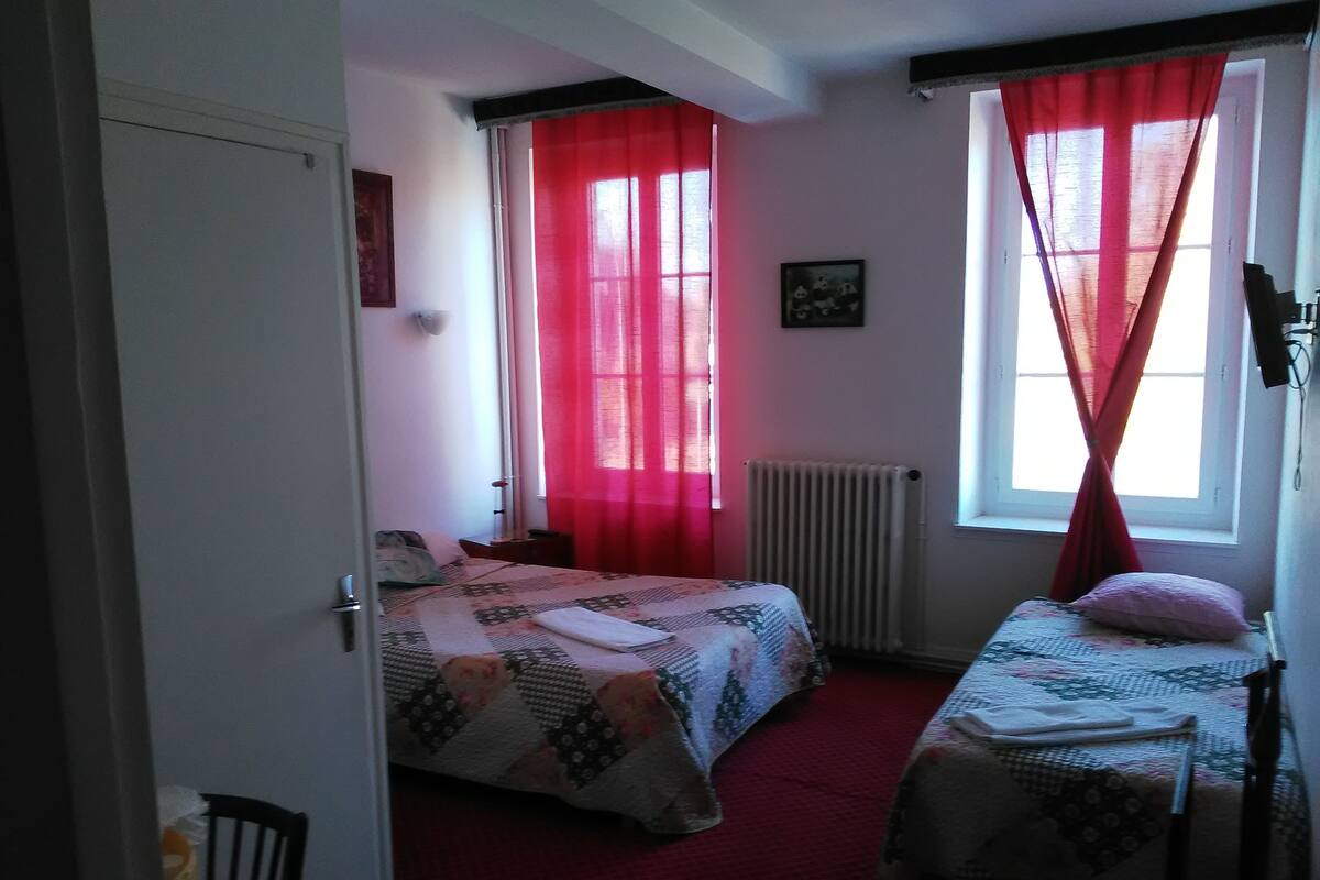 A bedroom with two beds, red curtains, a radiator, and a framed picture on the wall.