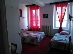 A bedroom with two beds, red curtains, a radiator, and a framed picture on the wall. - Le Relais de la Marche (Aigurande)