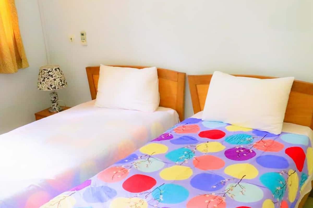 Une chambre avec deux lits, chacun recouvert d’une couvre-lit à motifs différents. Une table de chevet avec une lampe se trouve entre les deux lits.