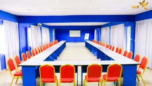 A conference room with a long table and red chairs, blue walls, and a projector screen. - Complexe Hôtelier Food And Business (Abidjan)
