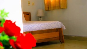 A bedroom with a bed, a bedside lamp, and a window with curtains. - Complexe Hôtelier Food And Business (Abidjan)