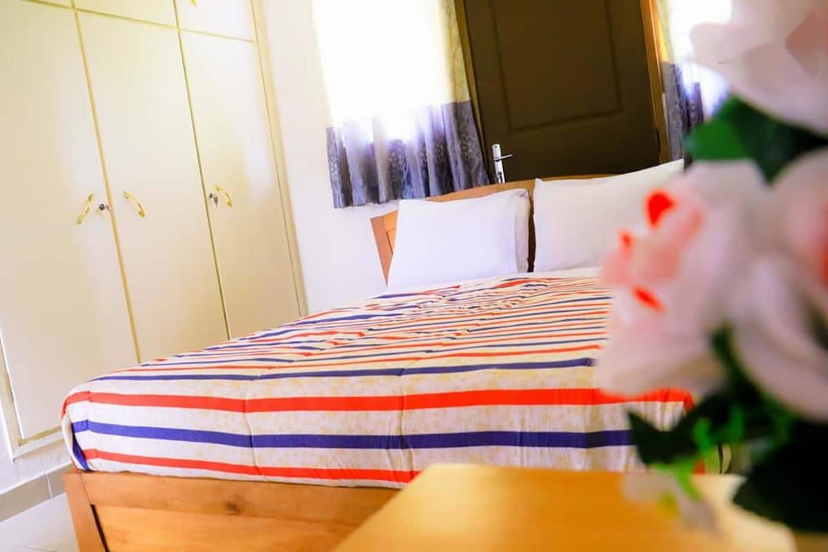 Une chambre à coucher avec une couvre-lit à rayures, une tête de lit en bois et un mur blanc avec une porte.