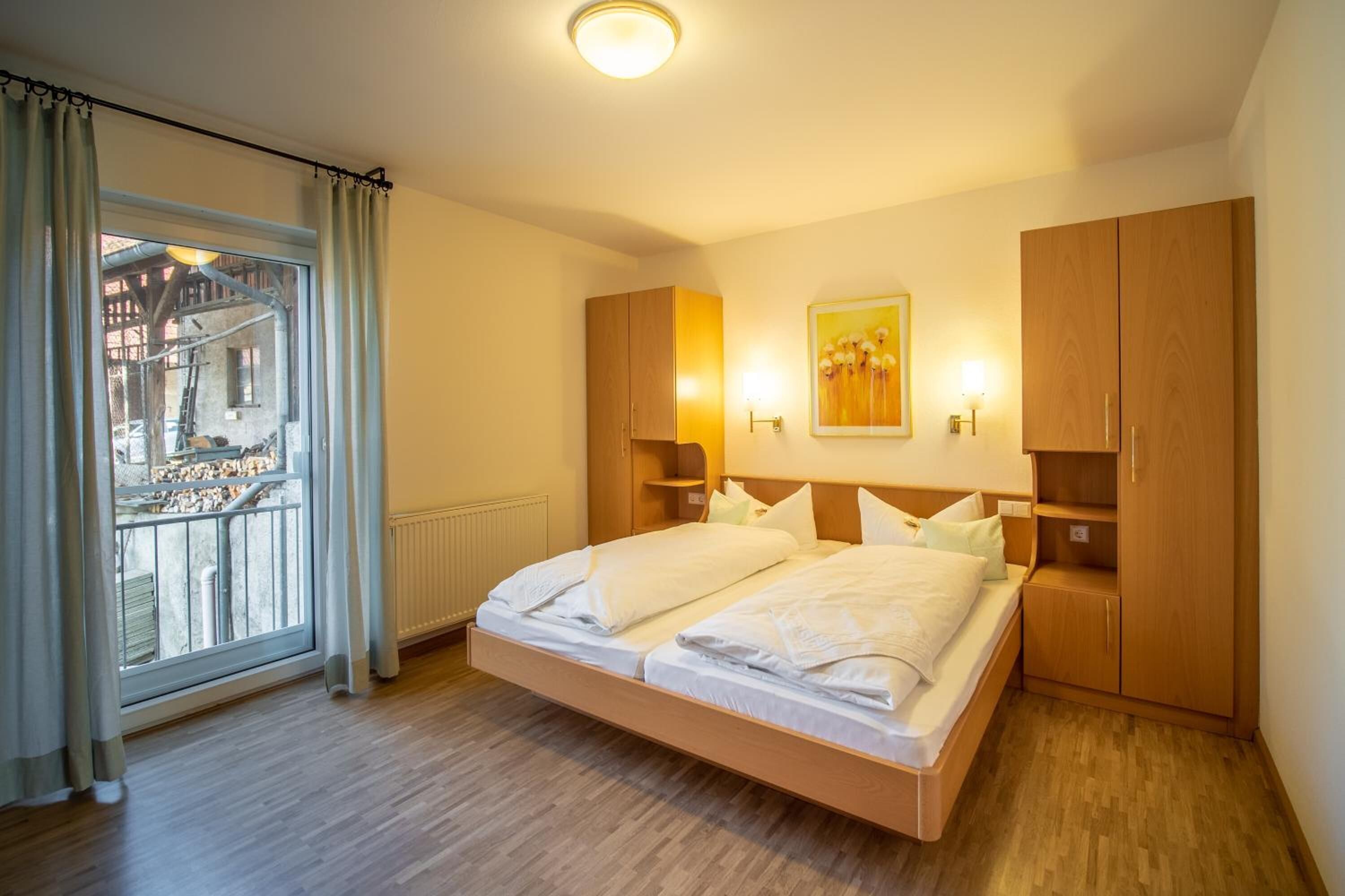 A modern bedroom with a large bed, wooden wardrobe, and a view of a building through a window.