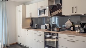 Una cocina moderna con armarios blancos, un horno de acero inoxidable, un microondas y una cafetera.