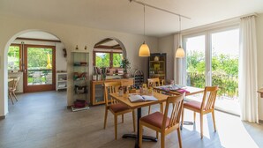Un comedor amplio con mobiliario de madera, una mesa central con libros y un menú, y ventanas grandes que ofrecen vistas al verdor.