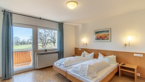 Una cama doble con sábanas blancas, una mesita de noche de madera, una pequeña mesa y un cuadro en la pared.