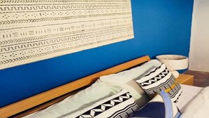 Un llit amb almofadines estampades, una paret blava i un panell de fusta al capçal.