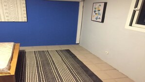 Habitació amb paret blava, una catifes amb dibuixos, un llit, un aparell d'aire condicionat i un quadre emmarcat.