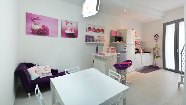 A modern kitchen with white cabinets, a dining area with a white table and purple sofa, and a small kitchenette. - A Casa Di CI (Acquaviva delle Fonti)