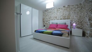 A bedroom with a stone wall, a bed with a colorful quilt, a nightstand with a lamp, and a wardrobe. - A Casa Di CI (Acquaviva delle Fonti)