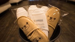 A bowl containing slippers with a bear design, labeled 'SLIPPERS', and a note indicating they are for guest use.