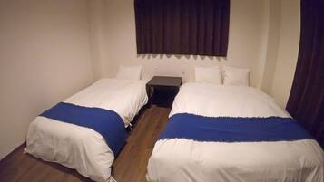 A room with two single beds, a small table, and a dark curtain.