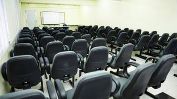 Un salón de conferencias con filas de sillas negras, una pizarra y una pantalla de proyector.