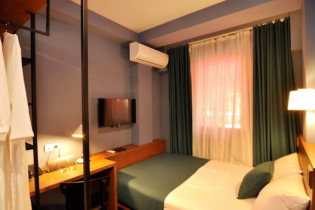 Ein Hotelzimmer mit einem Bett, einem Schreibtisch mit Computer, einem Fernseher und einer Klimaanlage.