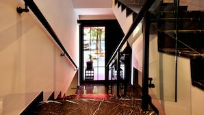 Un escalier avec des rampes noires et une porte en verre qui donne sur une pièce lumineuse offrant une vue sur l’extérieur.