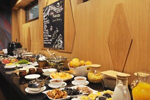 Ein Buffet mit einer Auswahl an Speisen und einer Schiefertafel, die Optionen wie Brot, Marmelade, Honig und Pfannkuchen auflistet.