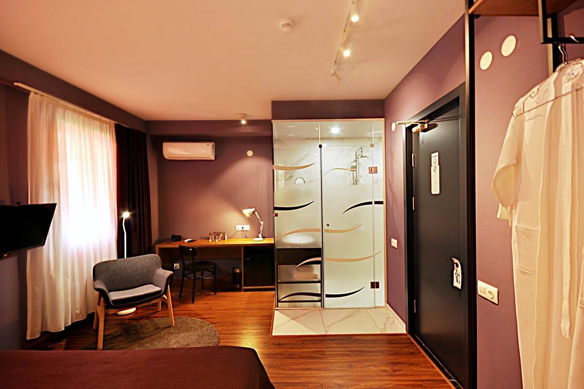 Ein Hotelzimmer mit Bett, Schreibtisch, Stuhl, Fernseher, Kleiderschrank und einem Badezimmer mit Glastür.