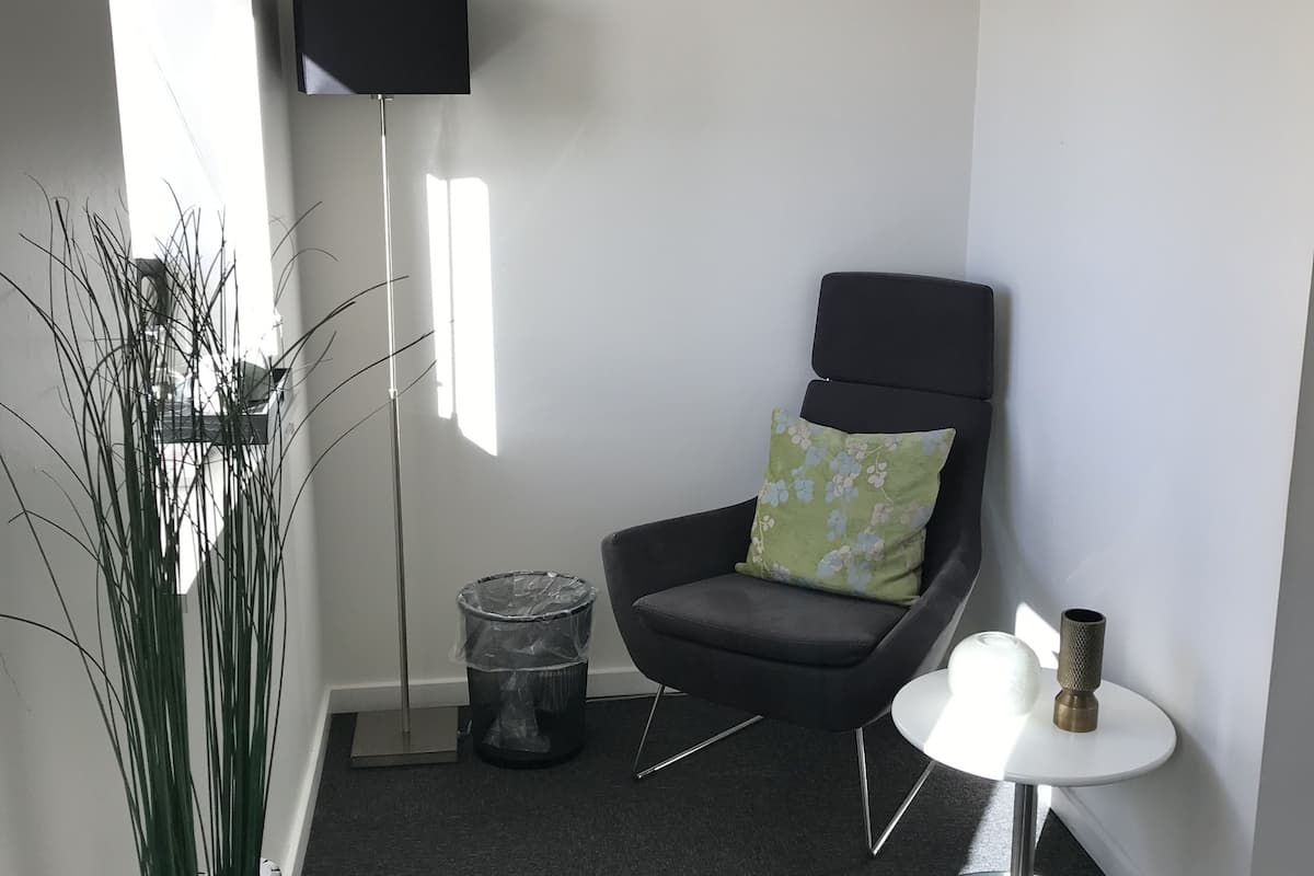 A modern living room with a dark grey armchair, a small round table, a floor lamp, and a trash bin.