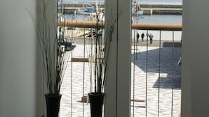 Een kamer met een groot raam met uitzicht op een strand, twee vazen op de vensterbank, en een uitzicht op zee en strand.