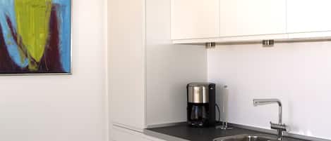 A modern kitchen with white cabinets, a stainless steel sink, and a coffee maker.
