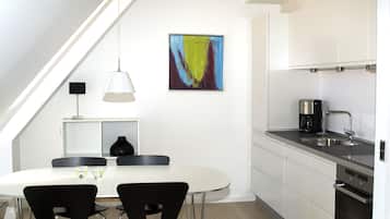 A modern kitchen with white cabinets, a dining table with two chairs, a coffee maker, and a painting on the wall.