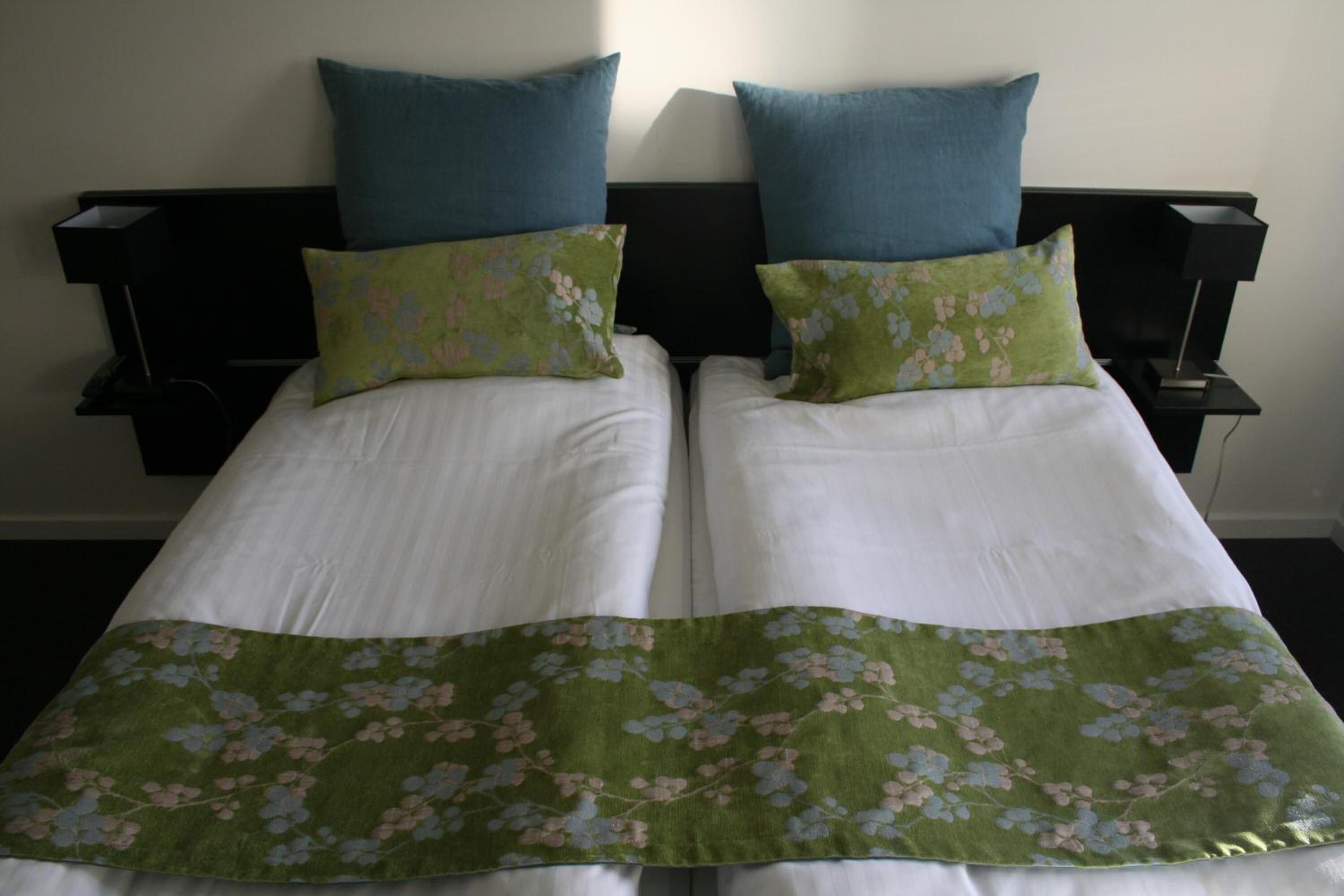 Un letto matrimoniale con biancheria bianca e copriletto floreale verde, affiancato da due cuscini blu.