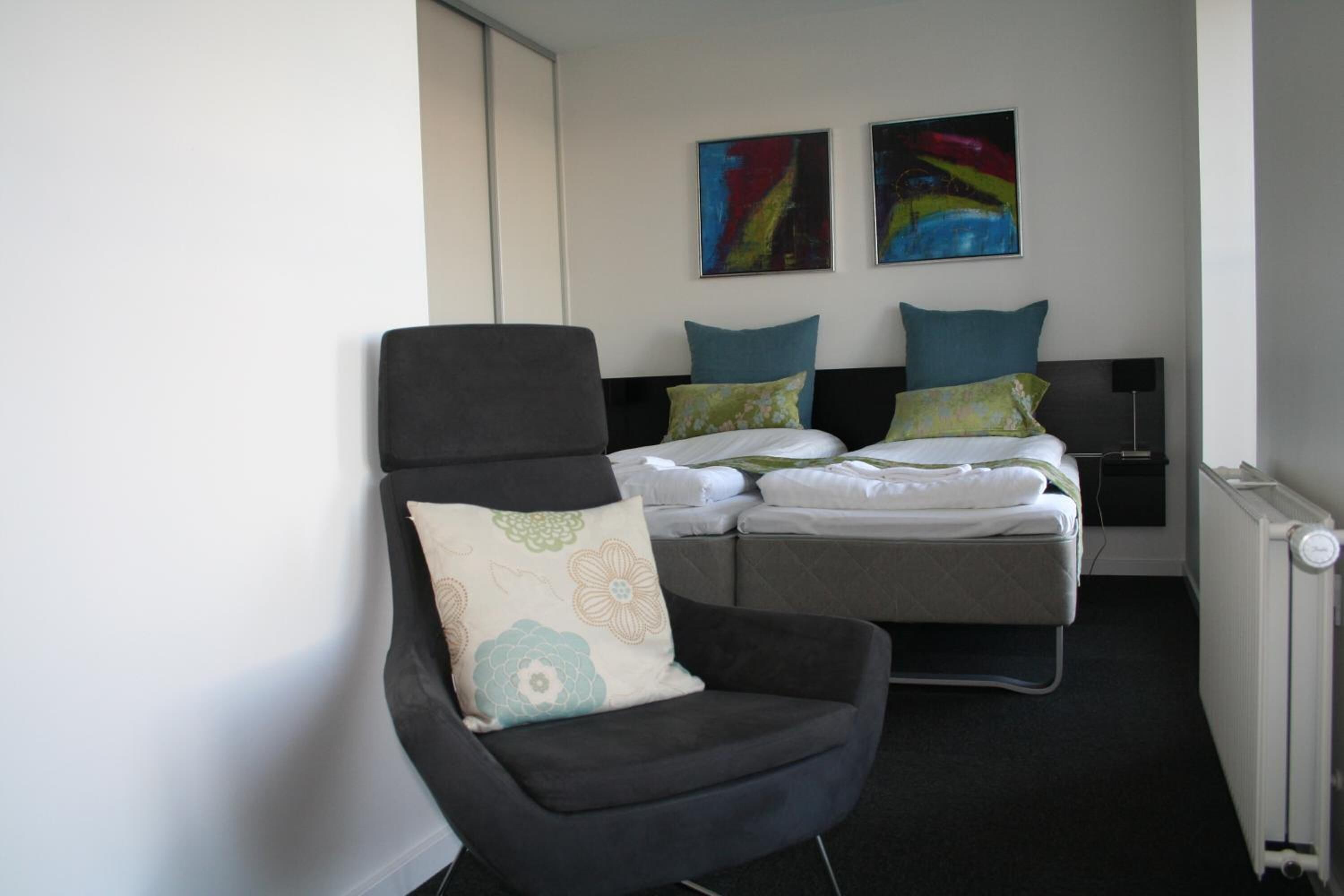 Une chambre d’hôtel avec un lit, une chaise et deux tableaux accrochés au mur.