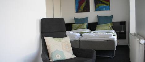 Una habitación de hotel con una cama, una silla y dos cuadros en la pared.