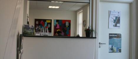 A reception area with a sign above a mirror, a door with a poster, and two lit lanterns on the floor.
