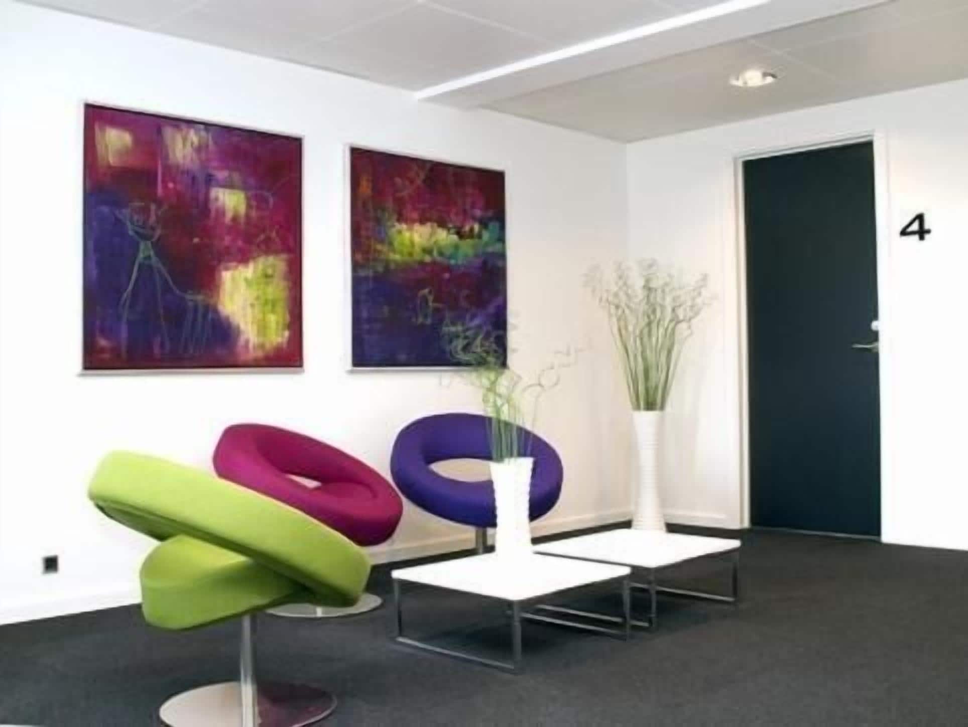 A modern office space with abstract paintings, a black door, and colorful chairs.