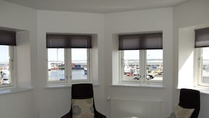 Een hotelkamer met een bed, twee stoelen, een tafeltje en drie ramen met uitzicht op een jachthaven.