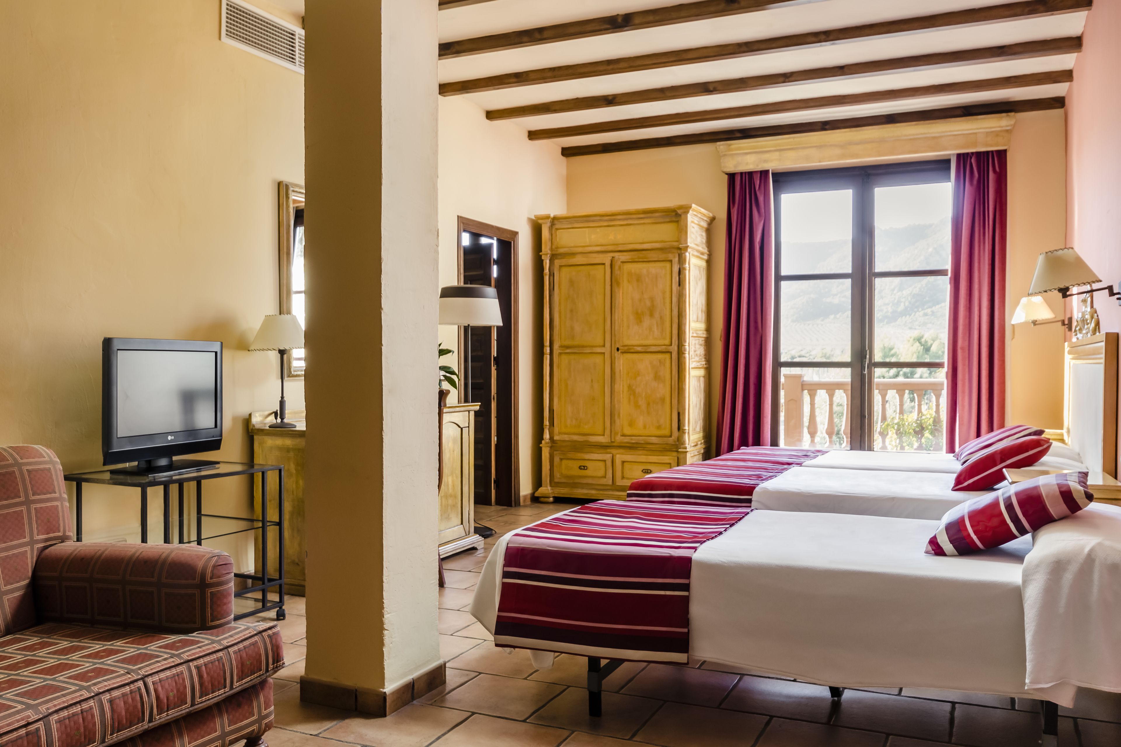 Habitación de hotel con dos camas, televisor, sofá y vistas al exterior.