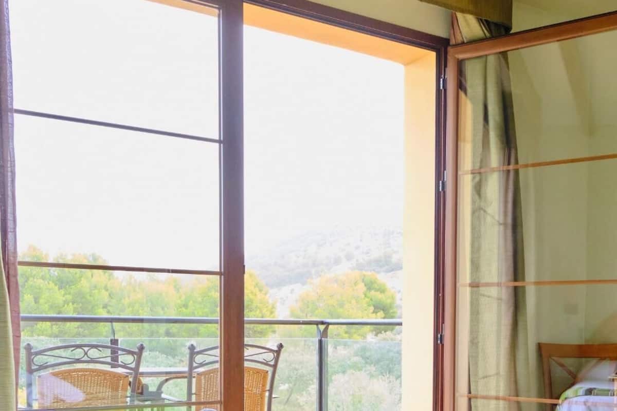 A hotel room with two beds, a balcony with a view of the countryside, and a table with chairs outside.