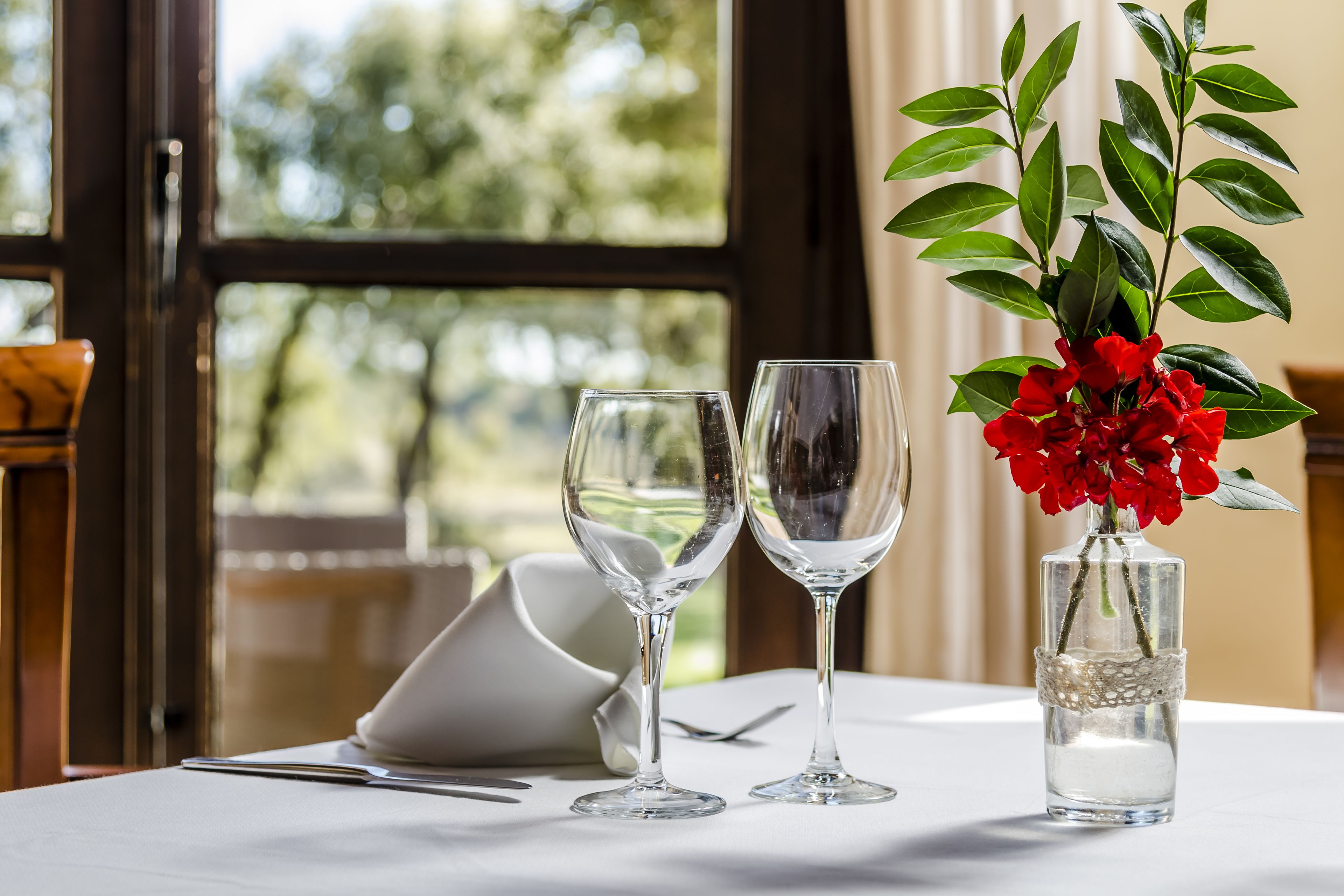 A table with two empty wine glasses and a small vase with red flowers.