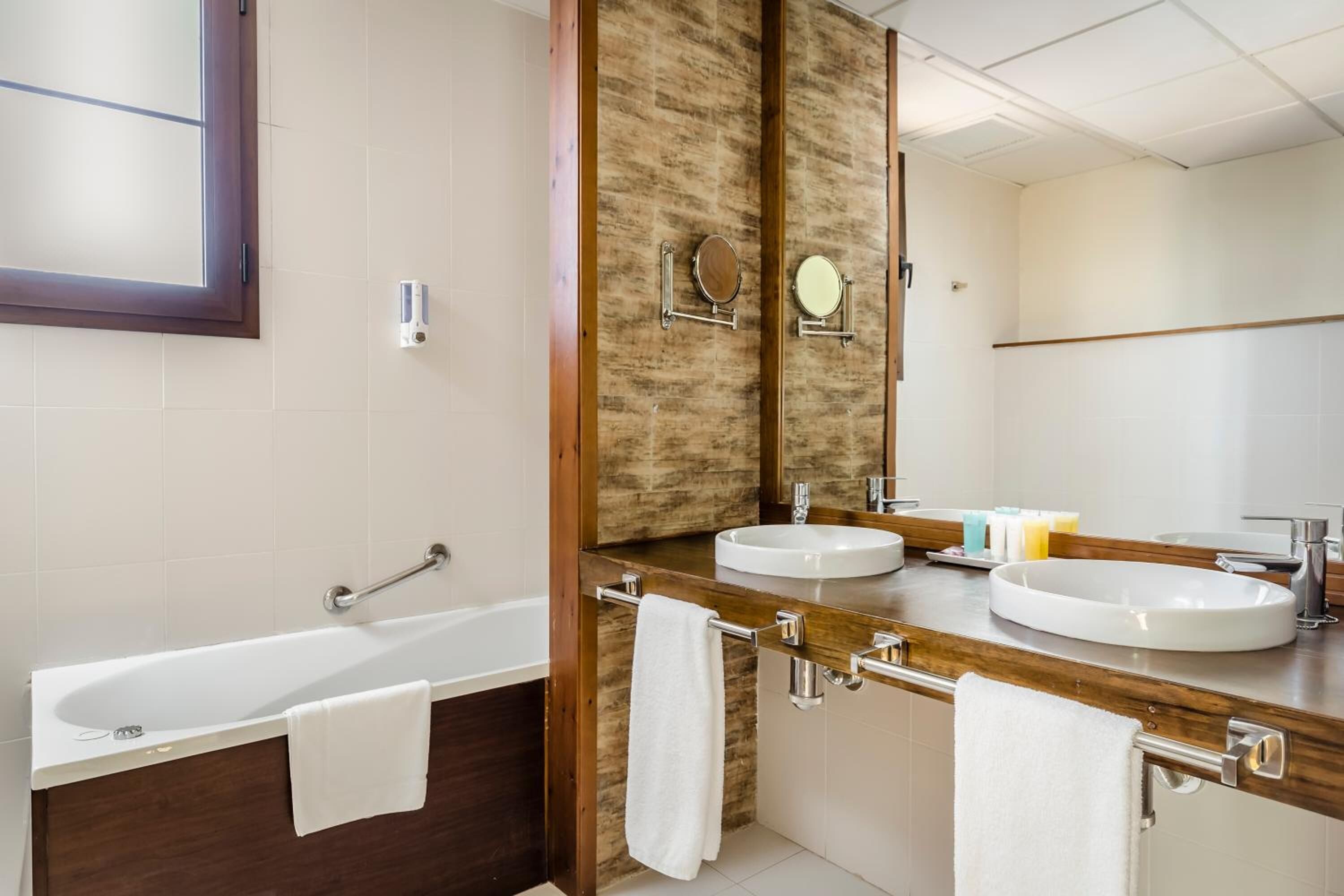 Un baño moderno con dos lavamanos, una bañera y un espejo grande.