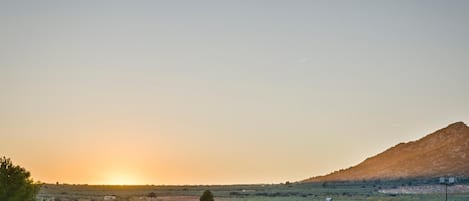Paisaje rural con atardecer, una colina y vegetación escasa.