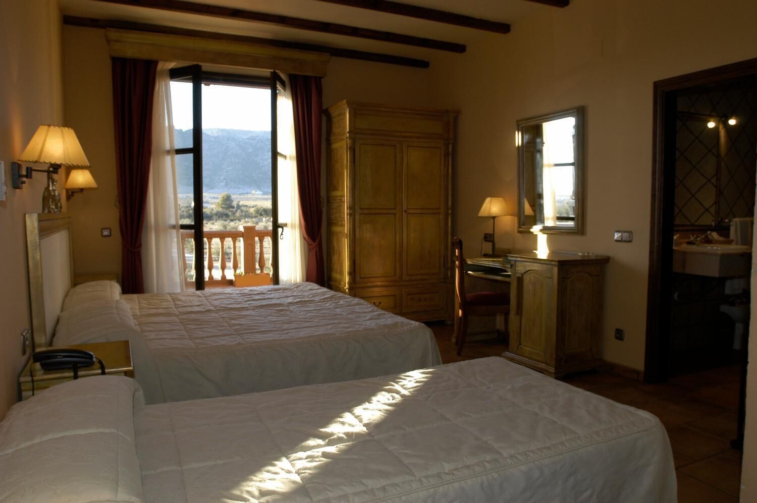 Une chambre d’hôtel avec deux lits, un bureau, une chaise, une armoire et un balcon avec vue.