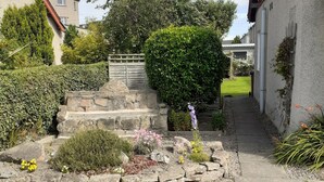 A residential garden with a stone pathway leading to a wooden gate, surrounded by various plants and flowers. - THE KEMPS Guest House (Inverness)