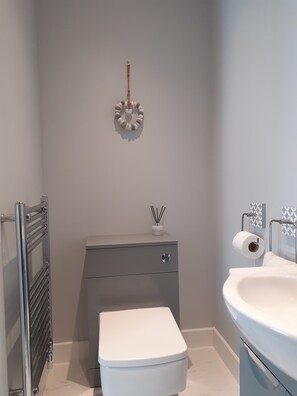 A bathroom with a white toilet, a sink, a towel rack, a small cabinet, and a wall-mounted toilet paper holder.