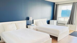 Habitación de hotel con dos camas, una mesita de noche, una lámpara y un ventanal con cortinas.
