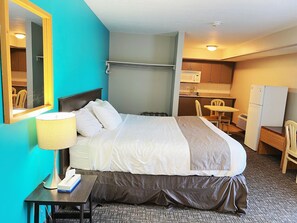 A hotel room with a bed, bedside table, lamp, and a kitchenette area with a microwave, refrigerator, and chair. - Riverside Inn (Wabasca-Desmarais)