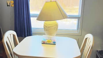 A small room with a table and two chairs, a window with a view of trees, a lamp, and a book on the table.