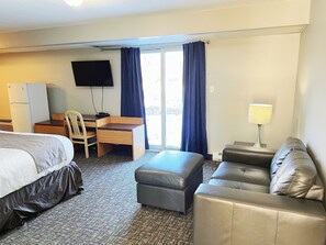 A hotel room with a bed, a desk with a chair, a sofa, a TV, and a lamp. - Riverside Inn (Wabasca-Desmarais)