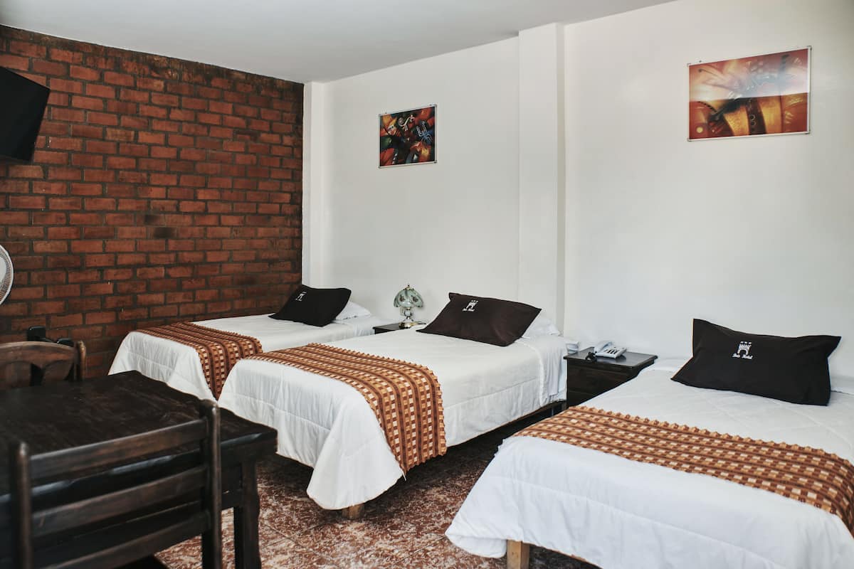 A hotel room with two single beds, a brick wall, and a small table with chairs.