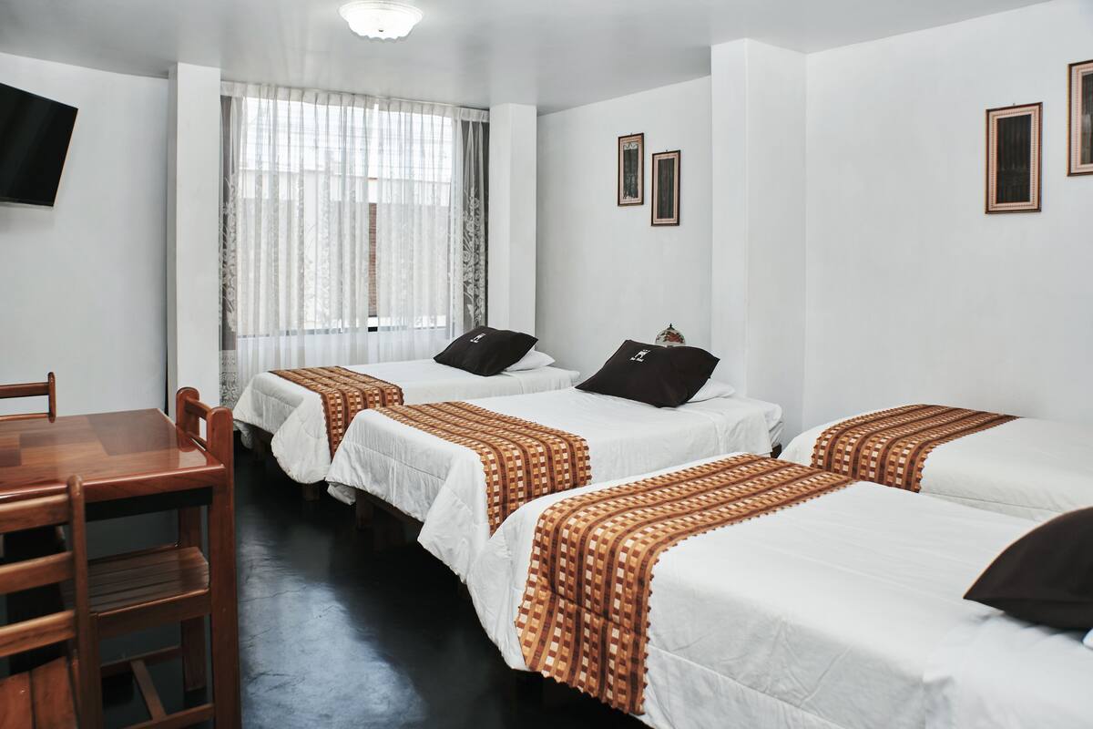 A hotel room with four single beds, a wooden table, and a TV mounted on the wall.