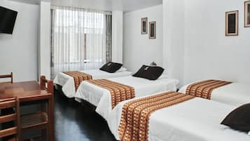Una habitación de hotel con cuatro camas individuales, una mesa de madera y un televisor montado en la pared.