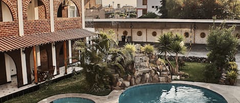 Una piscina con borde curvo, rodeada por un edificio de ladrillo con ventanas de arco y techo plano.